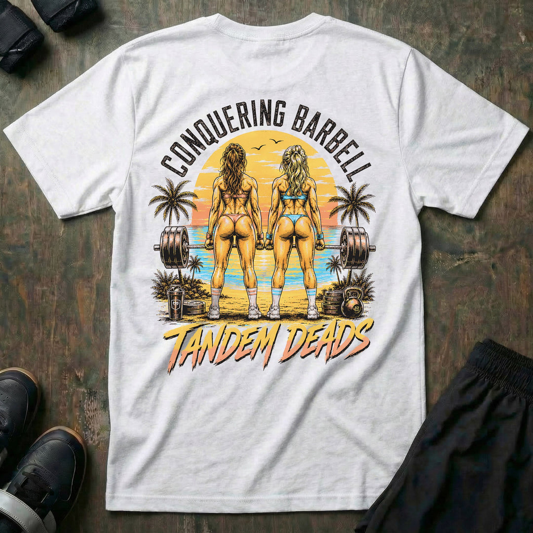 Tandem Deads tee in White: two athletic women deadlifting side by side on a palm-lined beach at sunset