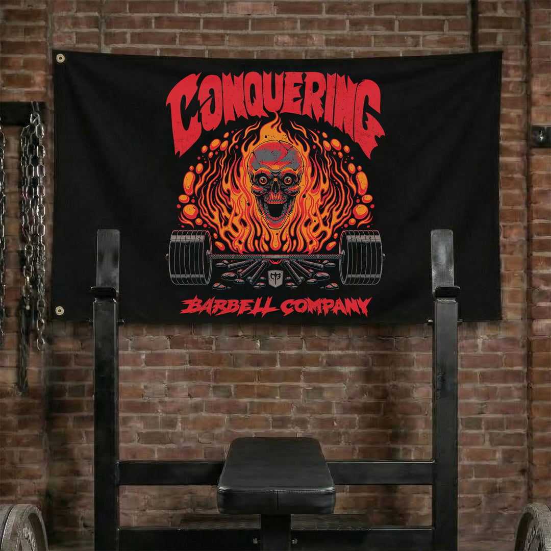 The Flaming Skull - Polyester Flag, horizontal black gym flag with skull engulfed in orange flame over a barbell - Conquering Barbell