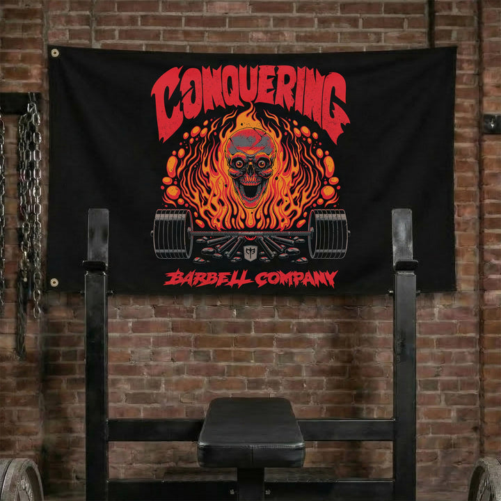 The Flaming Skull - Polyester Flag, horizontal black gym flag with skull engulfed in orange flame over a barbell - Conquering Barbell