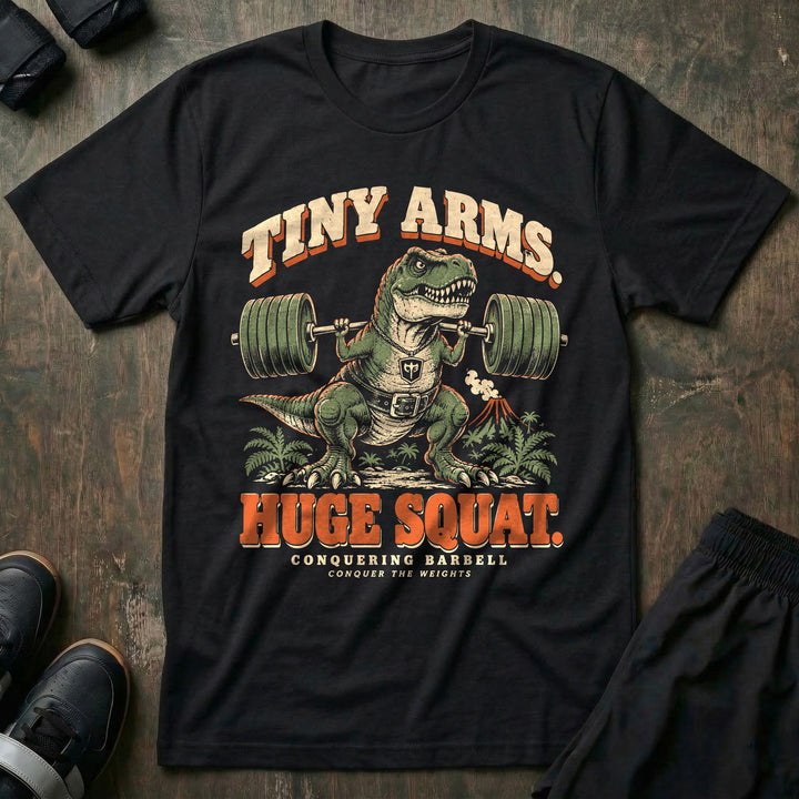 Tiny Arms Huge Squat - Tee front graphic in Black with a T. rex in a lifting belt squatting a loaded barbell with tiny arms - Conquering Barbell