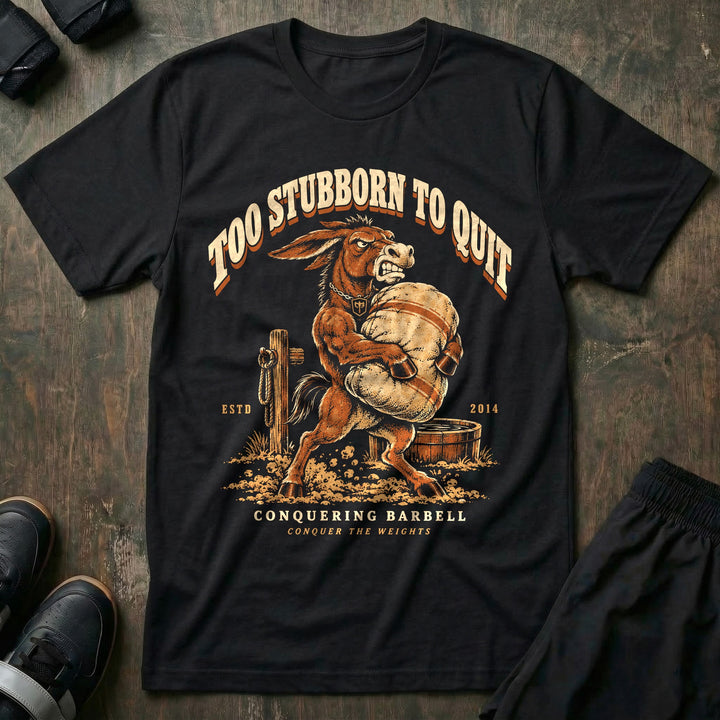 Too Stubborn to Quit - Tee front graphic in Black with a mule with teeth bared carrying a heavy sandbag - Conquering Barbell
