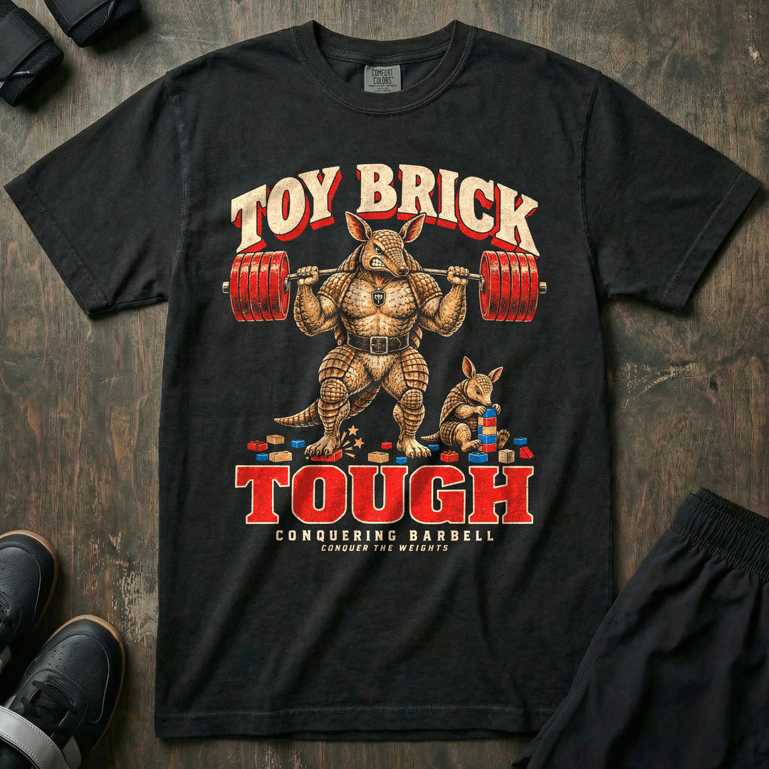 Toy Brick Tough - Relaxed Fit Tee front graphic in Black with an armadillo dad with a loaded barbell on his back stepping on a toy brick while a young armadillo stacks building blocks - Conquering Barbell