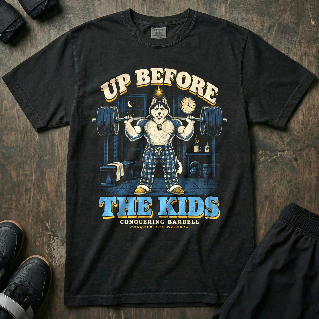 Up Before the Kids - Relaxed Fit Tee front graphic in Black with a husky dad in plaid pajama pants squatting a loaded barbell in a garage gym at night with a coffee mug and baby monitor on a shelf - Conquering Barbell
