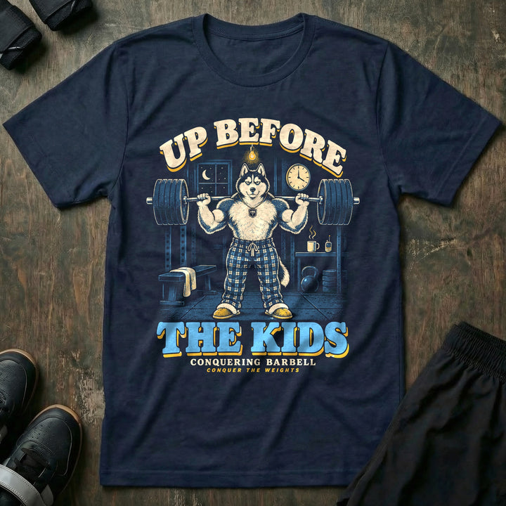 Up Before the Kids - Tee front graphic in Navy with a husky dad in plaid pajama pants squatting a loaded barbell in a garage gym at night with a coffee mug and baby monitor on a shelf - Conquering Barbell