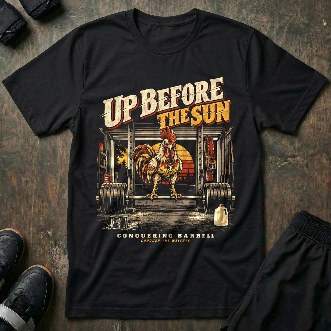 Up Before the Sun - Tee front graphic in Black with a rooster perched on a loaded barbell in a garage gym at sunrise - Conquering Barbell