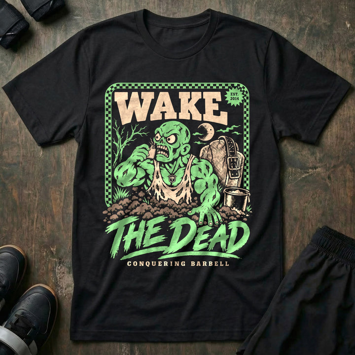 Wake the Dead V2 - Tee front graphic in Black with a zombie lifter climbing out of a grave sniffing smelling salts beside a tombstone with a lifting belt hung on it - Conquering Barbell