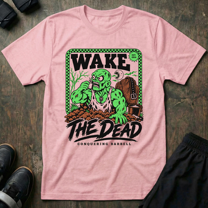 Wake the Dead V2 - Tee front graphic in Pink with a zombie lifter climbing out of a grave sniffing smelling salts beside a tombstone with a lifting belt hung on it - Conquering Barbell