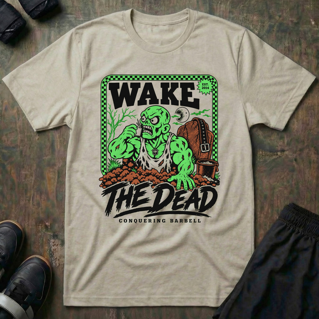 Wake the Dead V2 - Tee front graphic in Sand with a zombie lifter climbing out of a grave sniffing smelling salts beside a tombstone with a lifting belt hung on it - Conquering Barbell