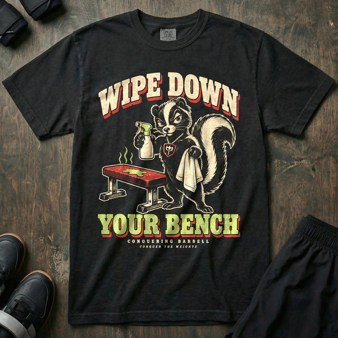 Wipe Down Your Bench - Relaxed Fit Tee front graphic in Black with a skunk with a spray bottle and towel glaring at a sweaty bench - Conquering Barbell