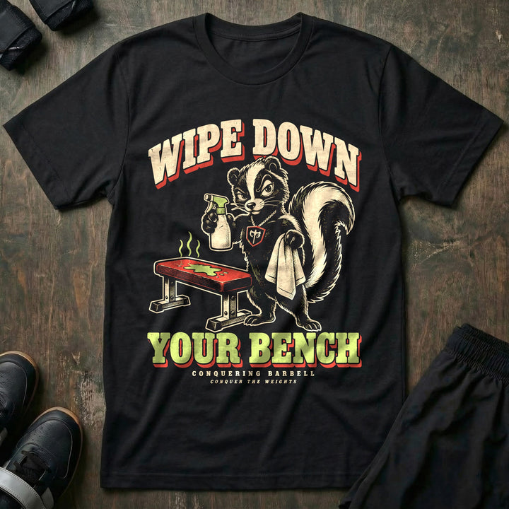 Wipe Down Your Bench - Tee front graphic in Black with a skunk with a spray bottle and towel glaring at a sweaty bench - Conquering Barbell
