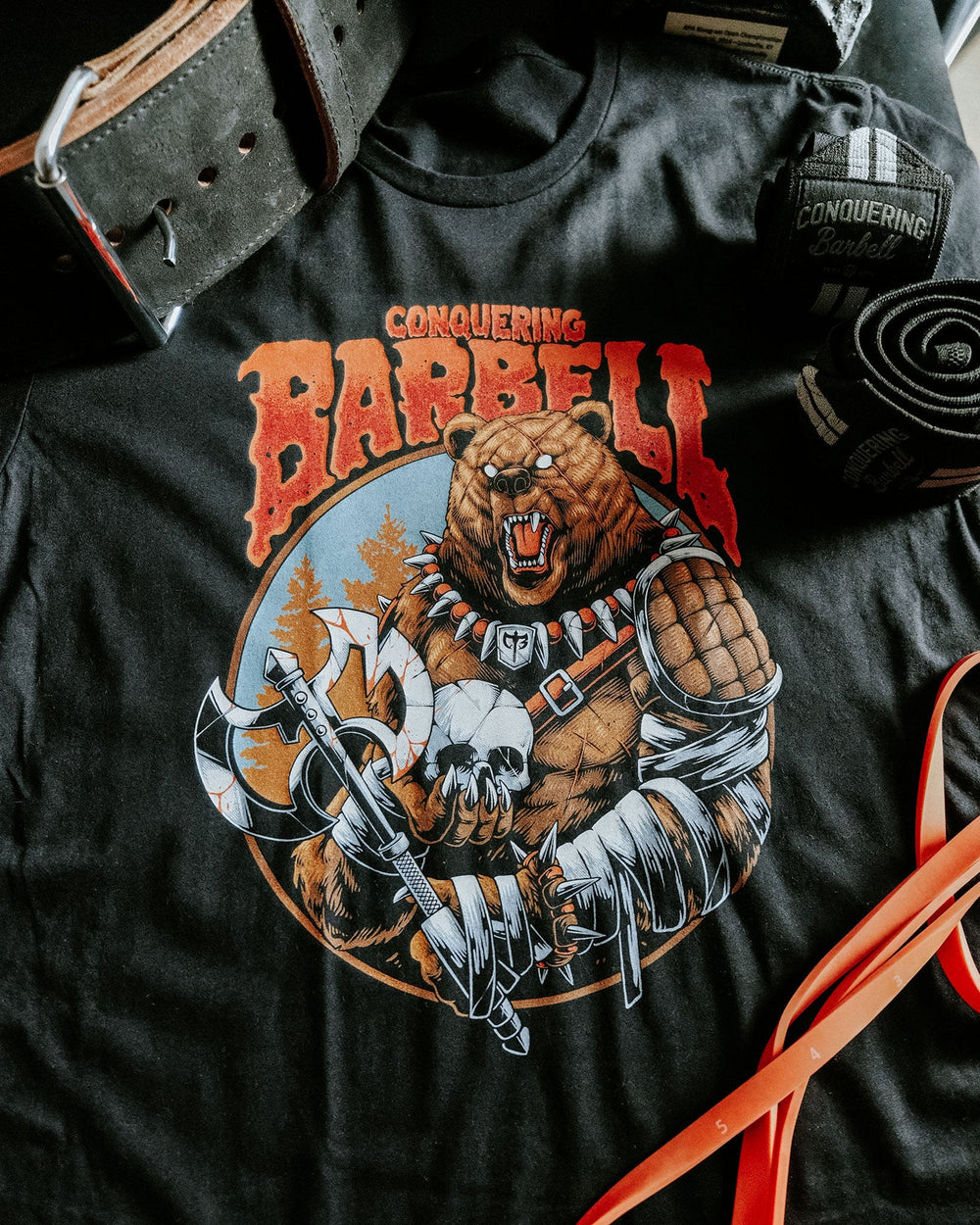 The Warrior Bear tee in Black: an armored grizzly viking warrior wielding twin axes with a skull at his belt
